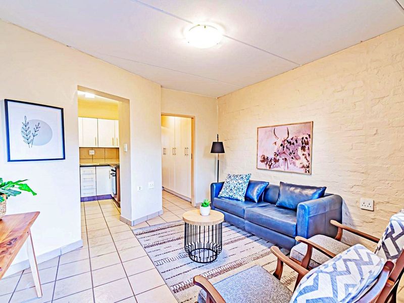 Open plan living area featuring tiled floors, an exposed brick feature wall, and direct access to the kitchen and hallway.