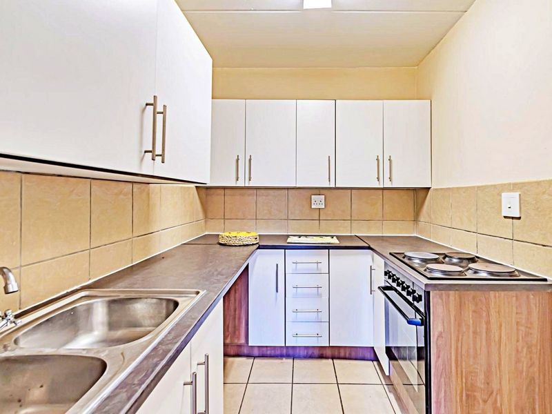 A functional galley-style kitchen featuring white cabinetry, laminate countertops, a double stainless steel sink, and a built-in electric stove and oven.