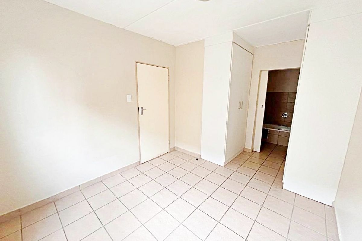 An empty bedroom featuring tiled flooring, a built-in wardrobe, and direct access to an en-suite bathroom.