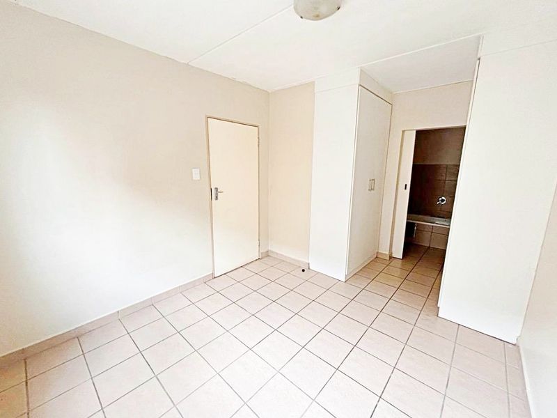 An empty bedroom featuring tiled flooring, a built-in wardrobe, and direct access to an en-suite bathroom.