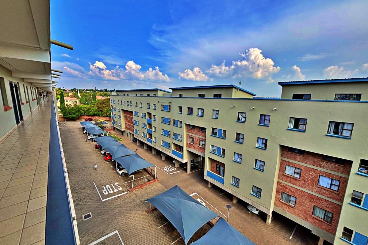 Elevated view of the apartment complex exterior, featuring a balcony walkway overlooking the parking area with shade-cloth carports.