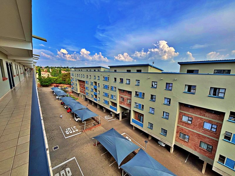 Elevated view of the apartment complex exterior, featuring a balcony walkway overlooking the parking area with shade-cloth carports.
