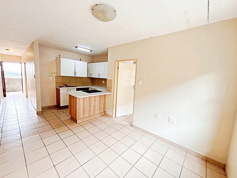 Open plan living area featuring tiled floors and a compact kitchen with built-in cabinetry and hob, leading to an outdoor balcony area.