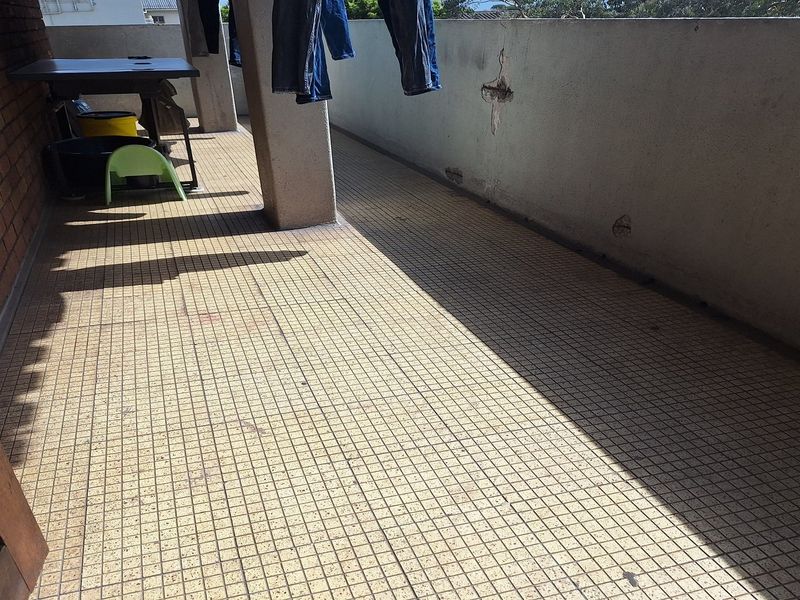 An outdoor balcony area featuring tiled flooring and a concrete balustrade, showing signs of wear and structural weathering.