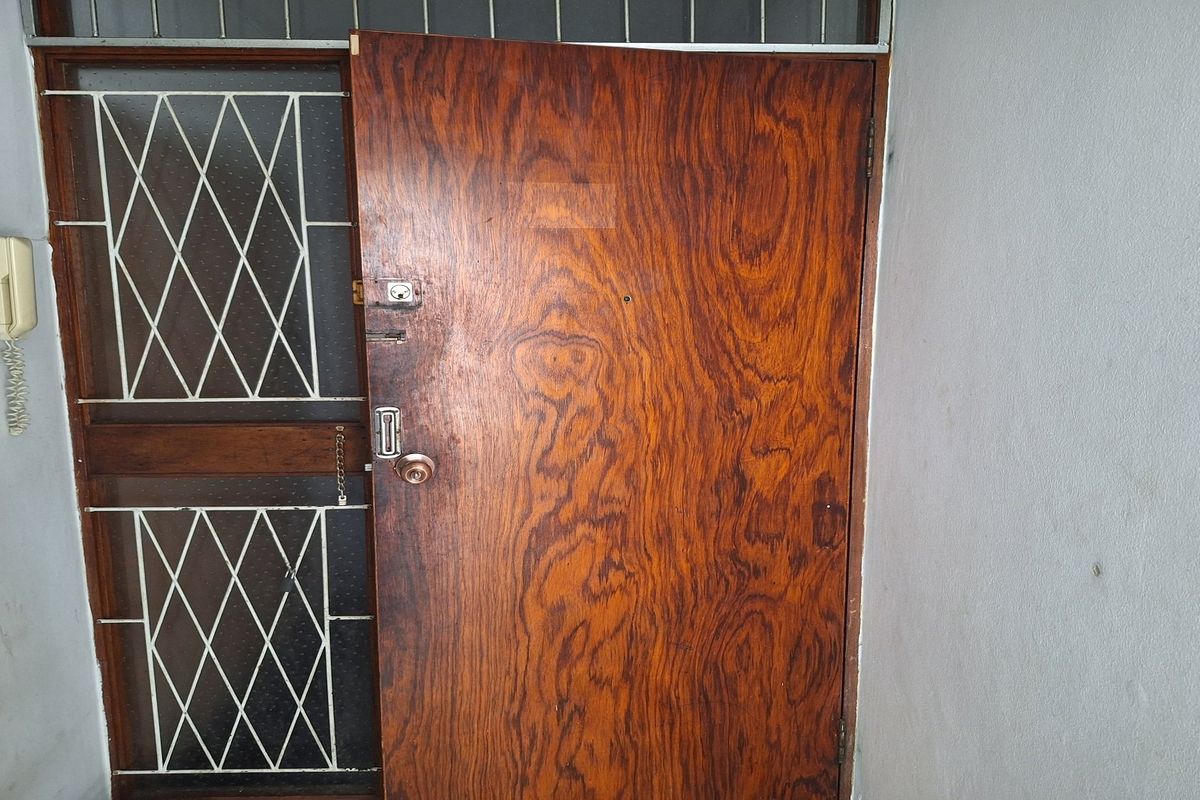 An apartment entrance featuring a wooden door and a security gate with an integrated intercom system.
