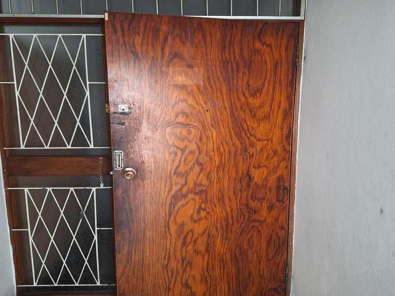 An apartment entrance featuring a wooden door and a security gate with an integrated intercom system.