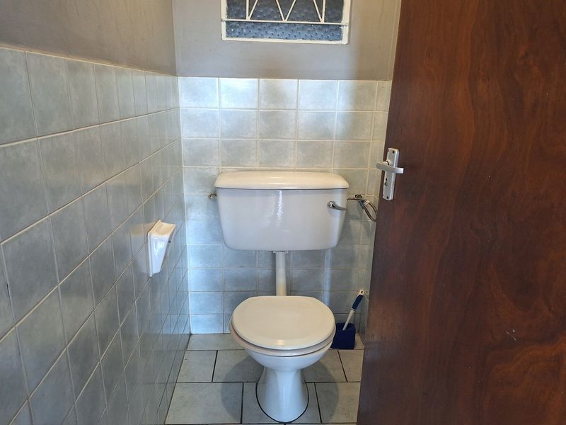 A compact bathroom featuring ceramic wall and floor tiling, a standard toilet, and a small high-level window for ventilation.