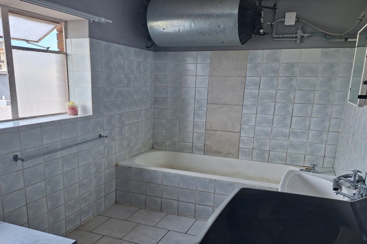 A dated bathroom featuring a built-in bathtub, tiled surfaces, and an exposed electric water heater, offering potential for modernization and renovation.