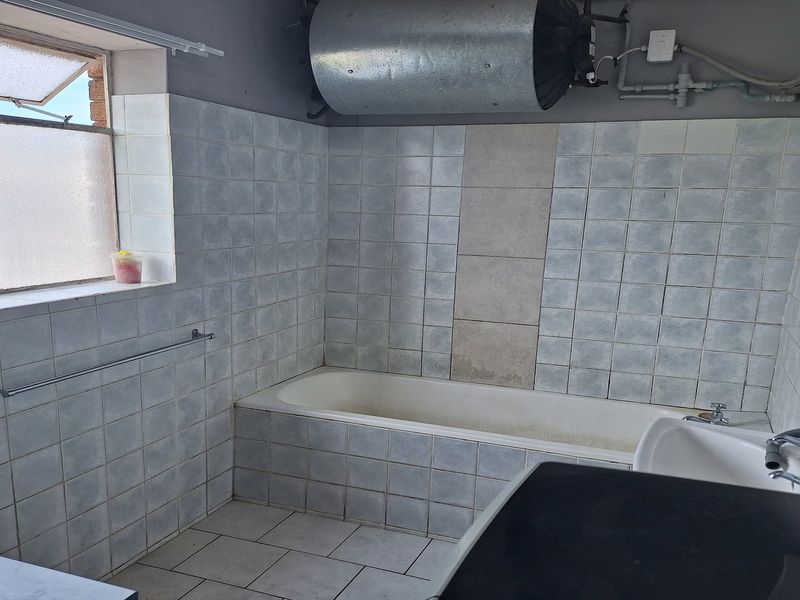 A dated bathroom featuring a built-in bathtub, tiled surfaces, and an exposed electric water heater, offering potential for modernization and renovation.