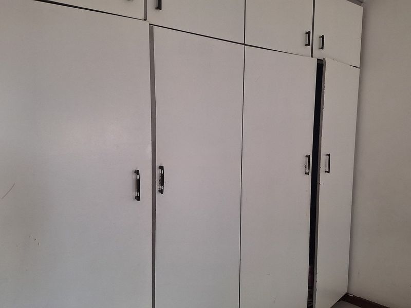 A bedroom featuring white built-in cupboards with visible wear and misaligned doors.