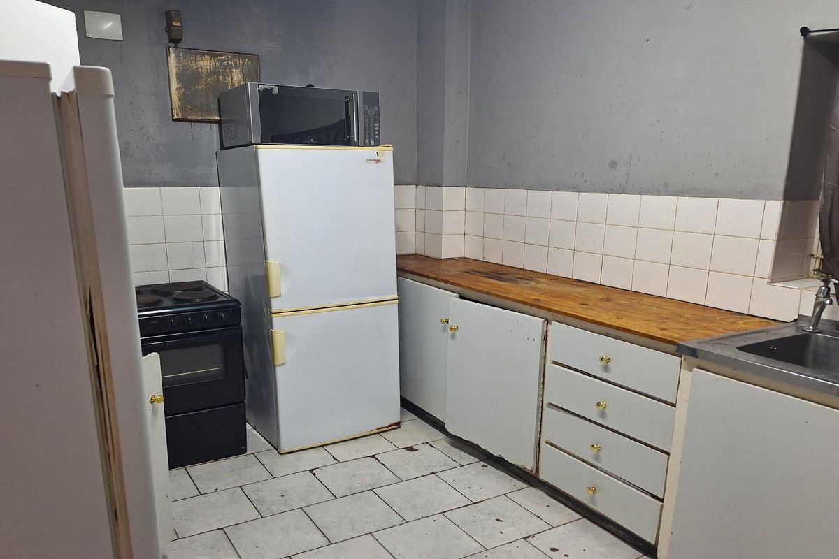 A dated kitchen featuring tiled flooring, a wooden countertop, and basic cabinetry, requiring modernization to improve its overall aesthetic and functionality.