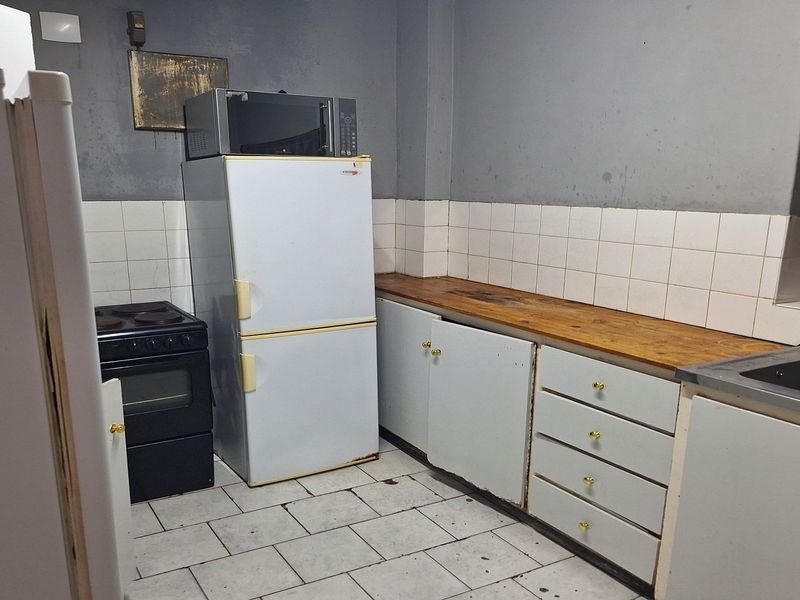 A dated kitchen featuring tiled flooring, a wooden countertop, and basic cabinetry, requiring modernization to improve its overall aesthetic and functionality.