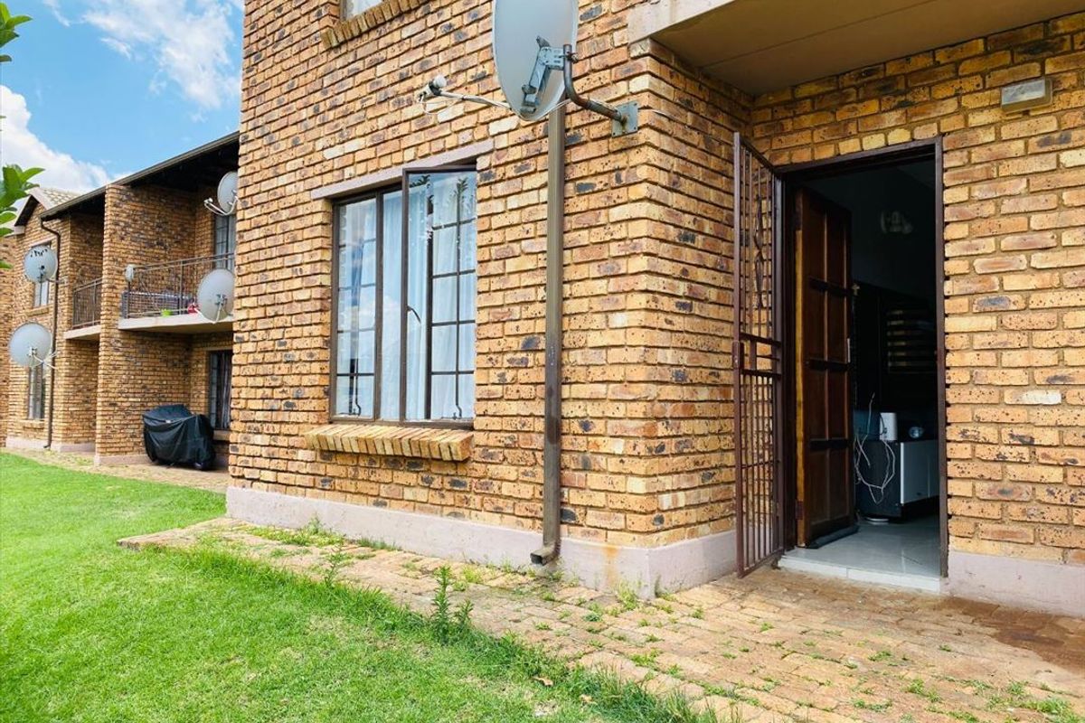 Rear view of a face brick townhouse featuring a paved walkway, lawn area, and security gate access to the interior.
