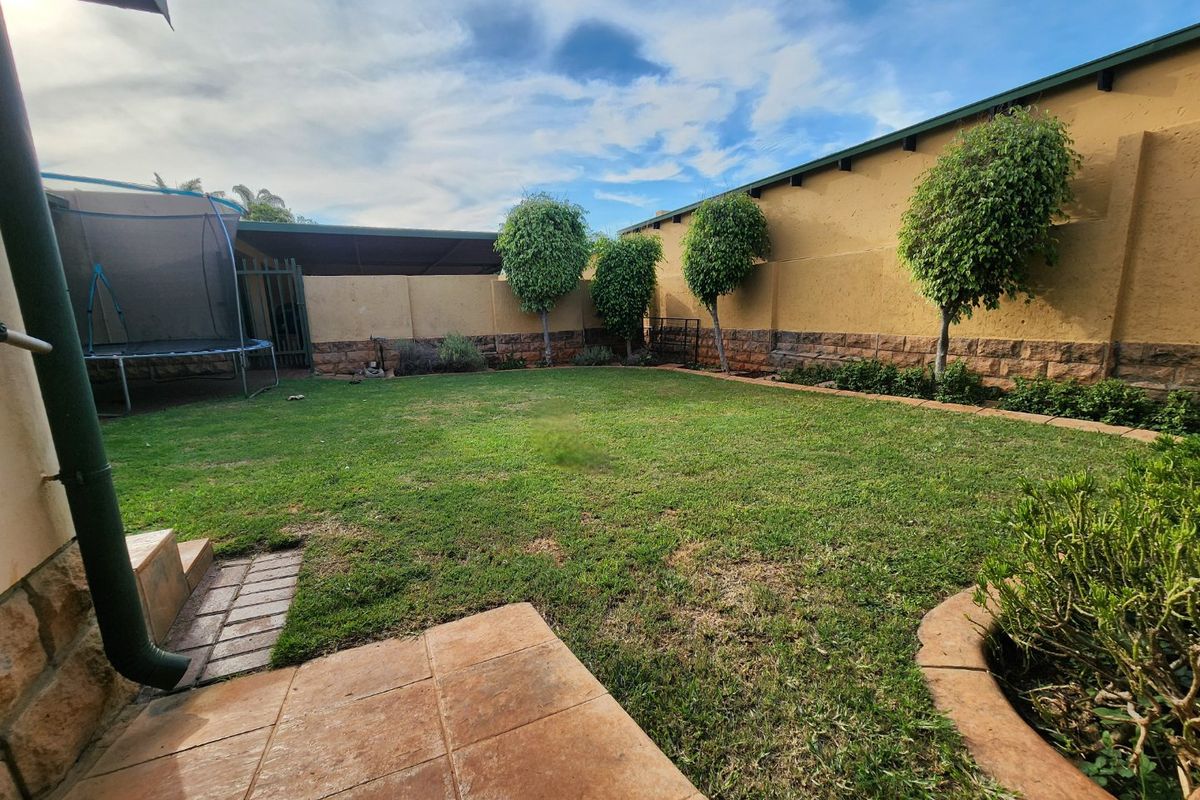 A private rear garden featuring a paved patio area, established trees, and a perimeter boundary wall.