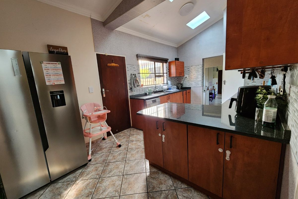 A functional kitchen featuring dark wood cabinetry, granite countertops, tiled flooring, and a vaulted ceiling with skylights providing natural light.