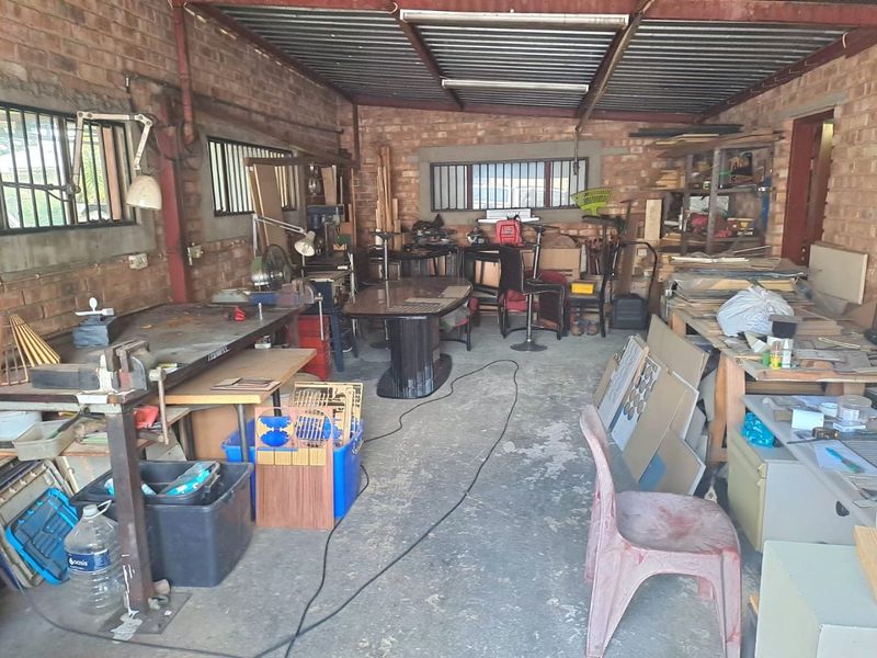 A functional garage space featuring exposed brick walls, corrugated metal roofing, and concrete flooring, currently utilized as a workshop area.