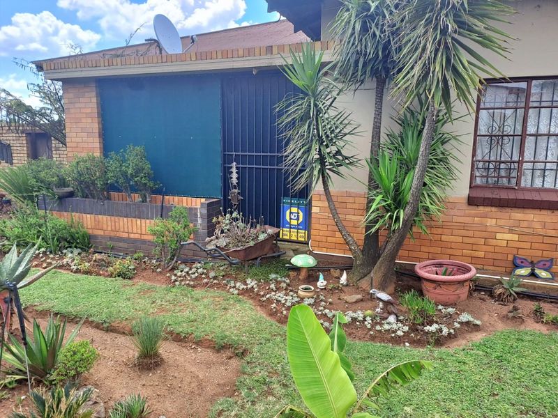 Front elevation of a brick house featuring a landscaped garden, security gate, and security bars on the windows.
