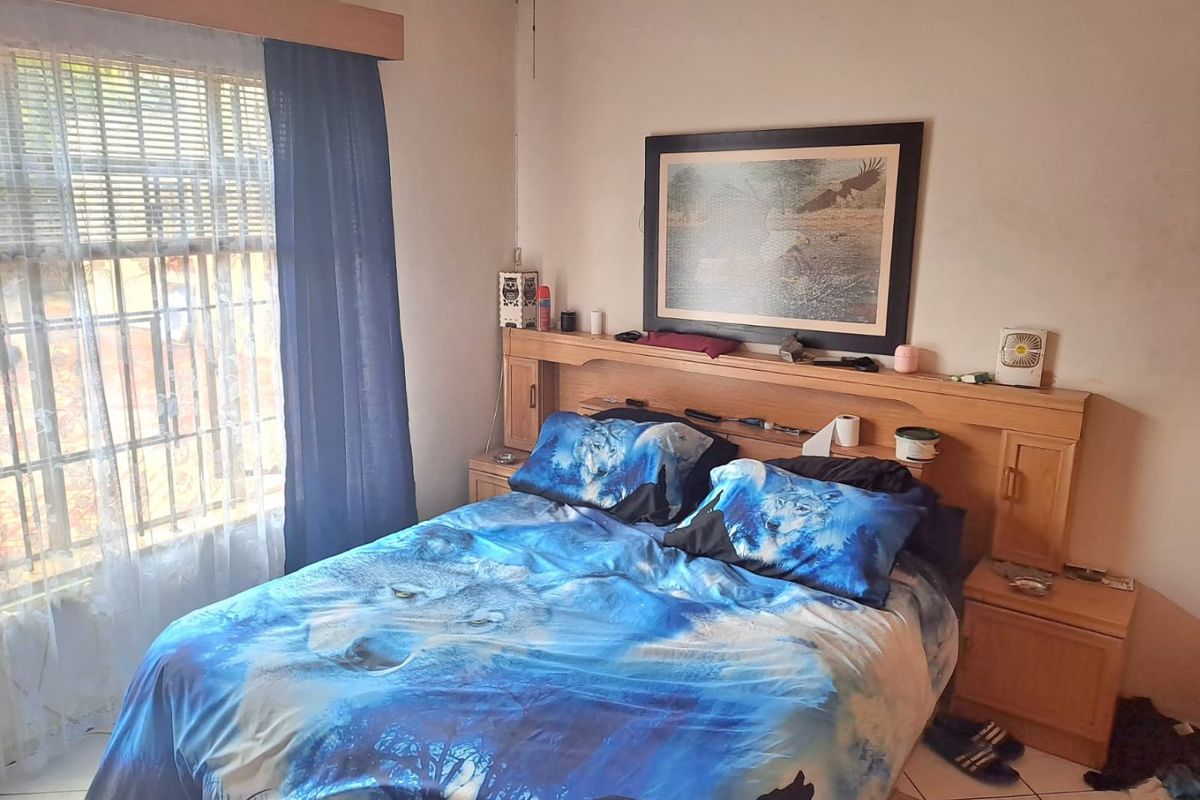 A bedroom featuring a built-in wooden headboard, tiled flooring, and security bars on the window. The room requires cosmetic updates to improve its overall condition.