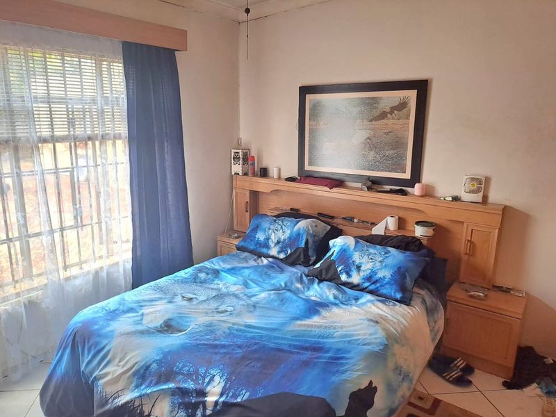 A bedroom featuring a built-in wooden headboard, tiled flooring, and security bars on the window. The room requires cosmetic updates to improve its overall condition.