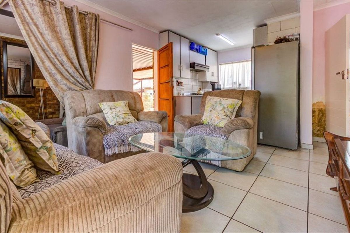 Open-plan living area featuring tiled flooring and an integrated kitchen space, showing signs of wall damage requiring maintenance.