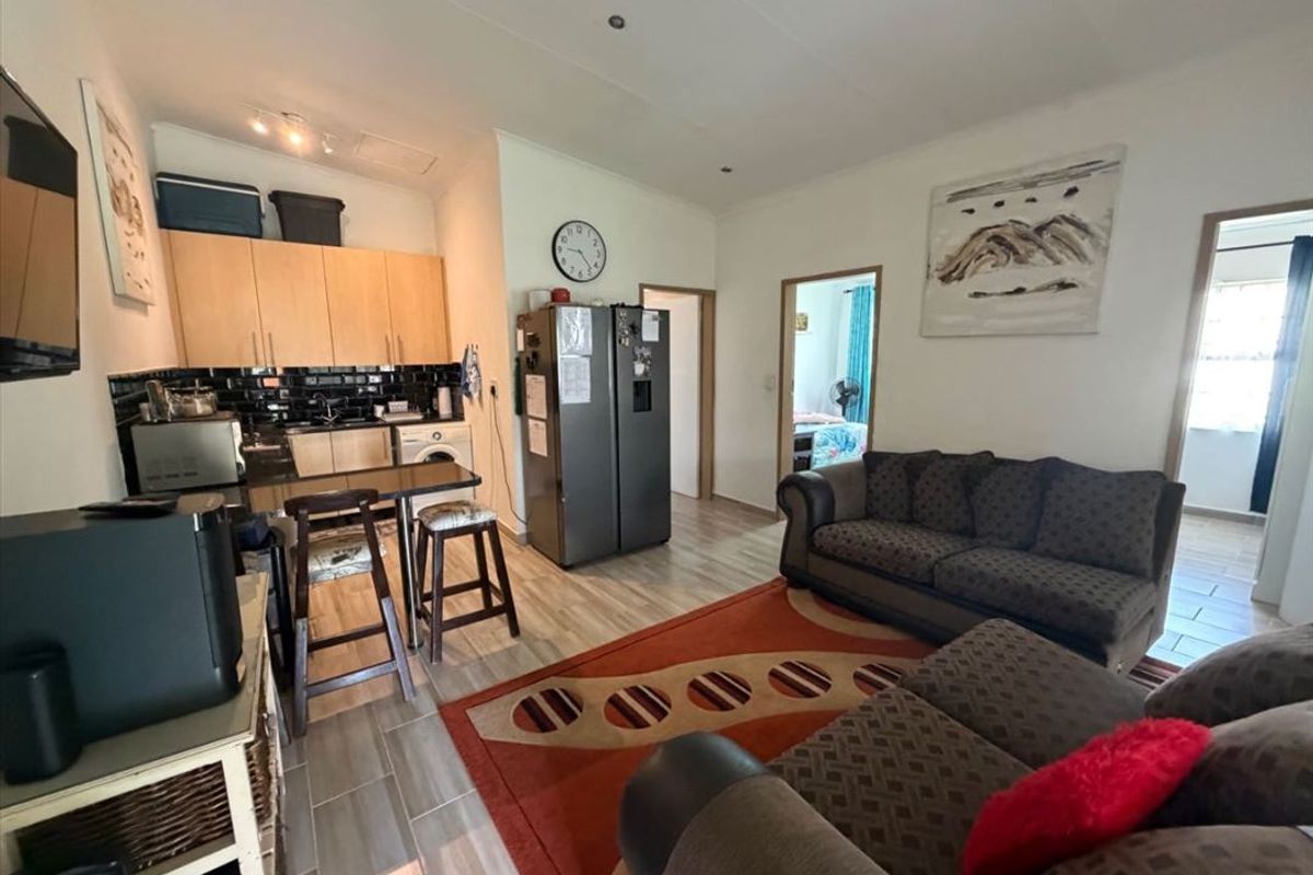 Open-plan living area featuring a compact kitchen with built-in cabinetry, black subway tile backsplash, and a breakfast bar, seamlessly connected to the lounge space.