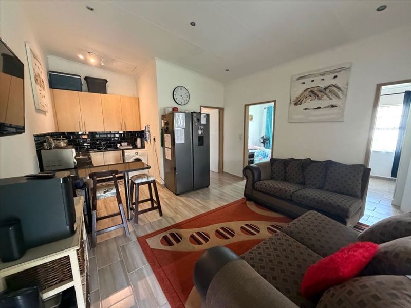 Open-plan living area featuring a compact kitchen with built-in cabinetry, black subway tile backsplash, and a breakfast bar, seamlessly connected to the lounge space.