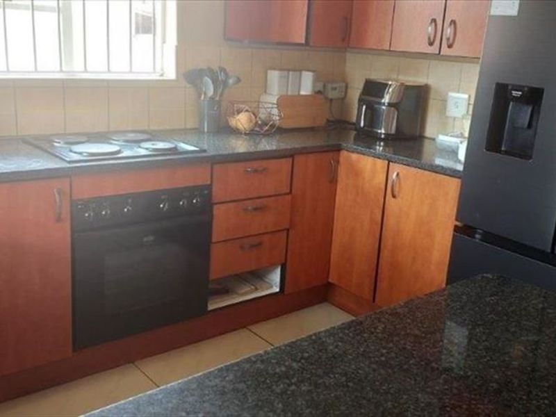 A functional kitchen featuring wood-finish cabinetry, granite countertops, a built-in oven, and an electric hob with a tiled backsplash.