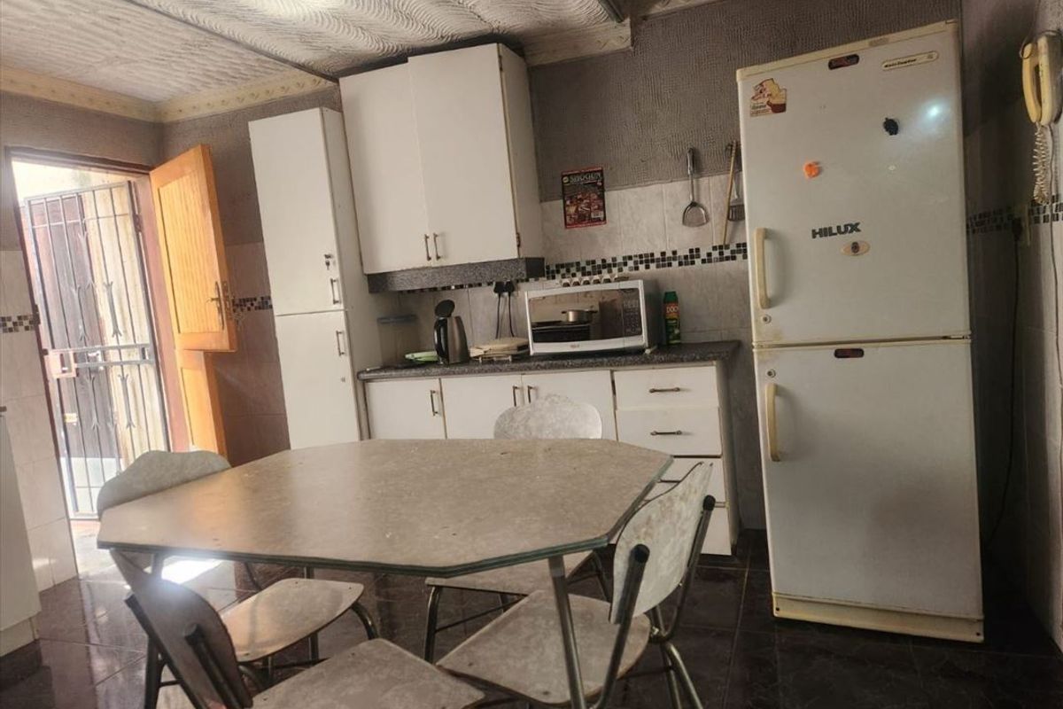 A functional kitchen area featuring built-in cabinetry, tiled backsplash, and direct access to an exterior area through a security gate.