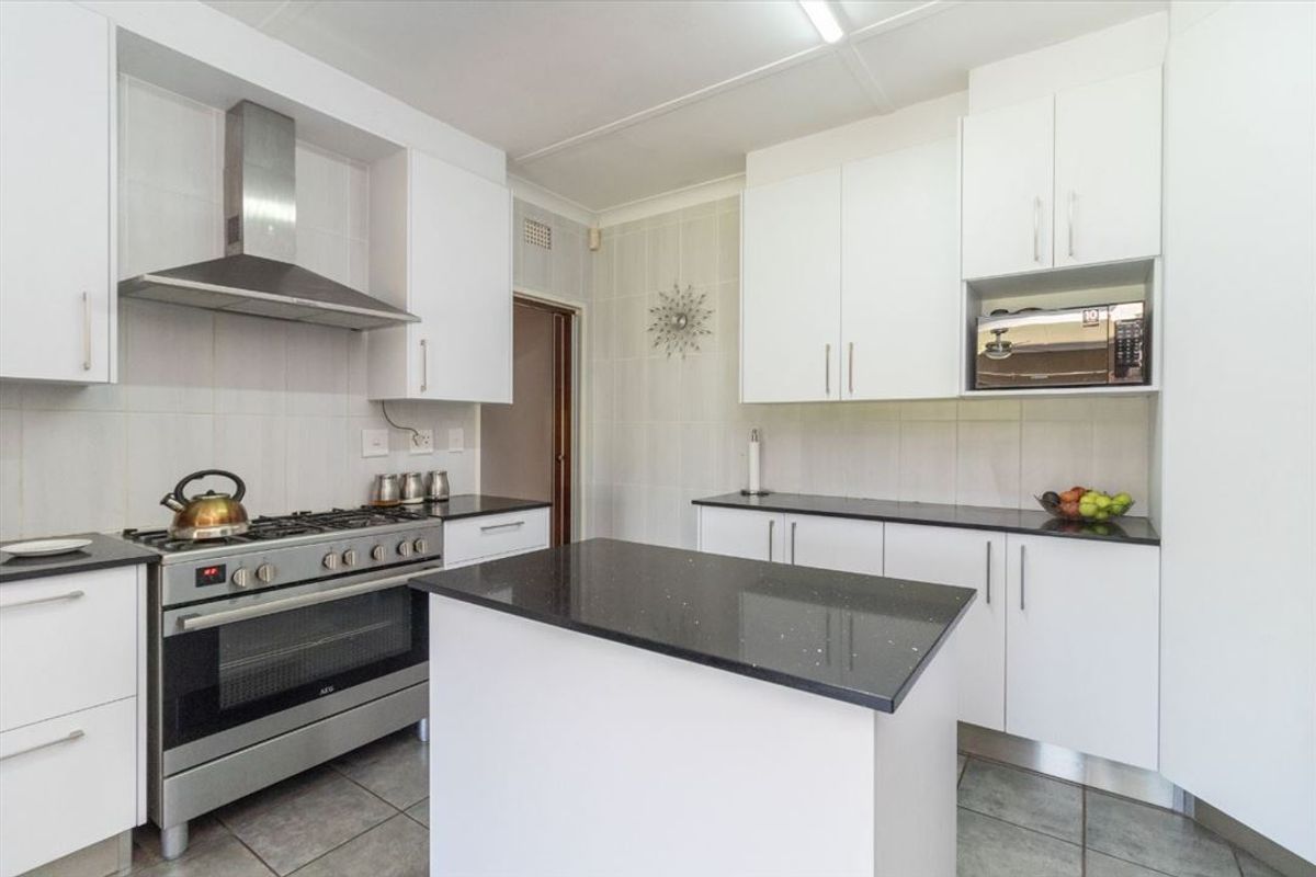 Modern kitchen featuring white cabinetry, granite countertops, a central island, and stainless steel appliances including a gas stove and extractor fan.