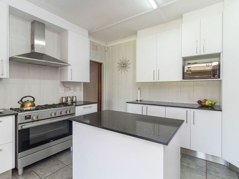 Modern kitchen featuring white cabinetry, granite countertops, a central island, and stainless steel appliances including a gas stove and extractor fan.