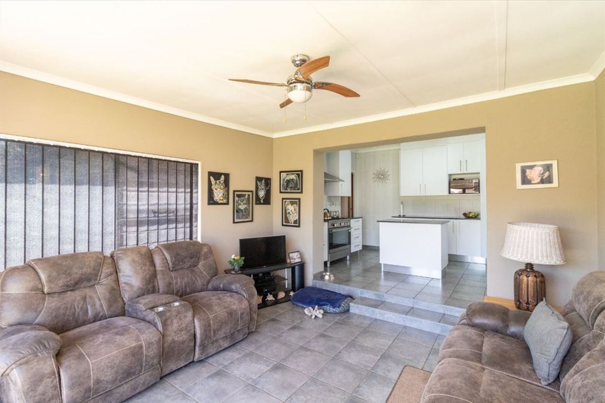 Open-plan living area featuring tiled floors, a ceiling fan, and a modern kitchen with white cabinetry and built-in appliances.