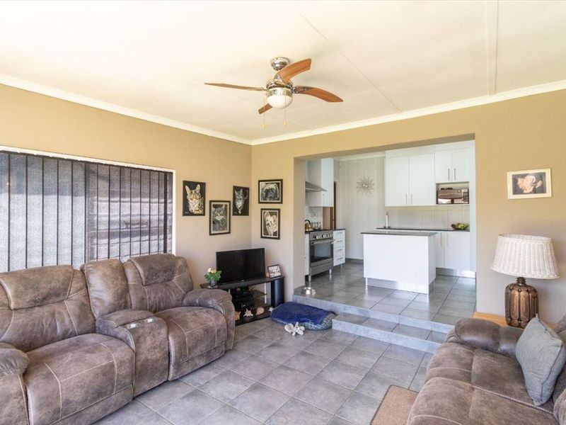 Open-plan living area featuring tiled floors, a ceiling fan, and a modern kitchen with white cabinetry and built-in appliances.