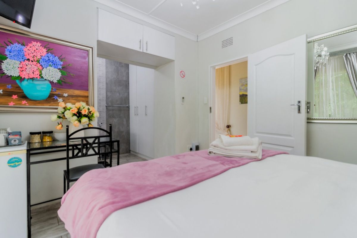 A well-maintained bedroom featuring built-in cupboards, overhead storage, and an adjoining en-suite bathroom area with modern grey tiling.