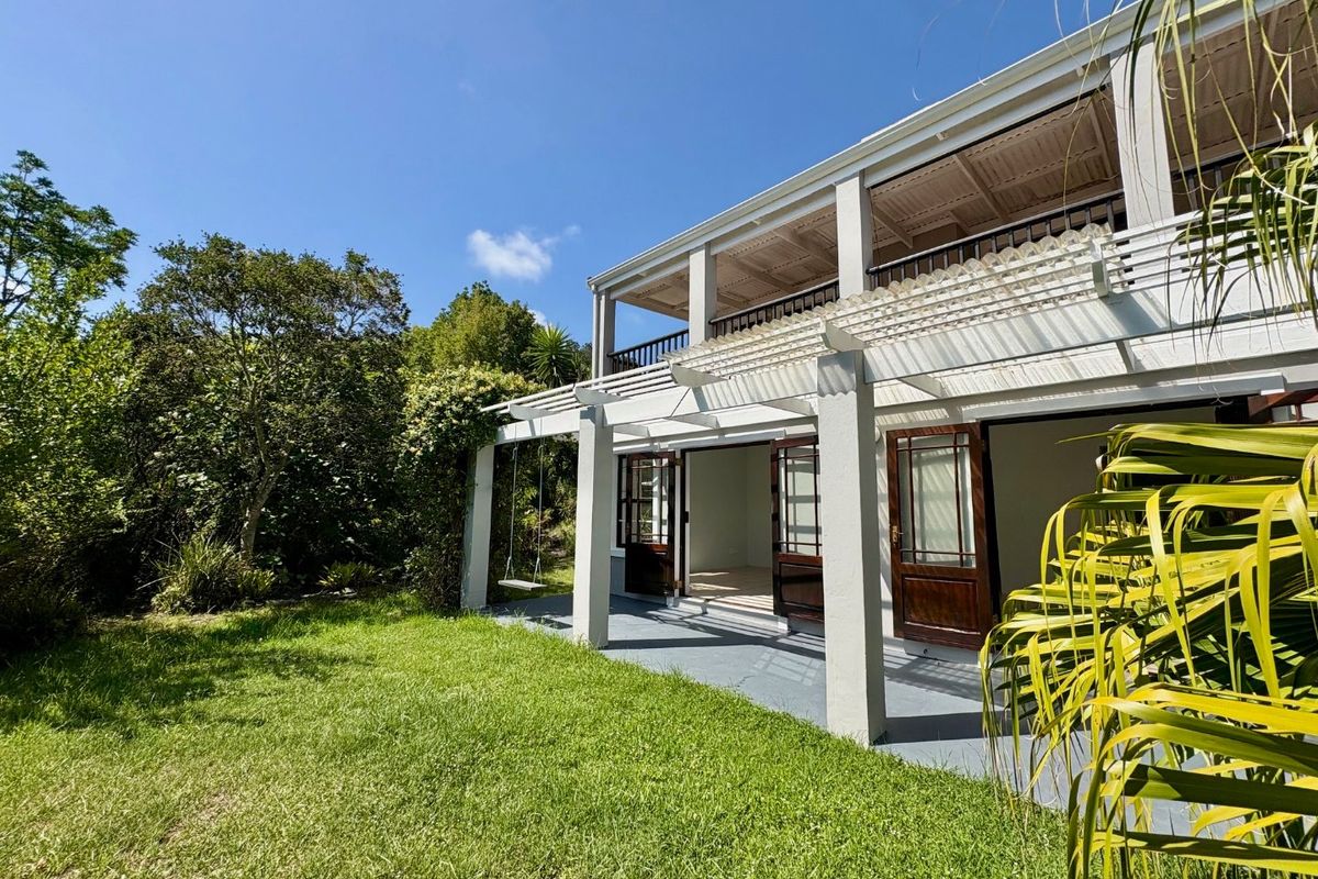 Rear view of the property featuring a covered patio with a pergola, upper-level balcony, and direct access to the garden through timber-framed doors.
