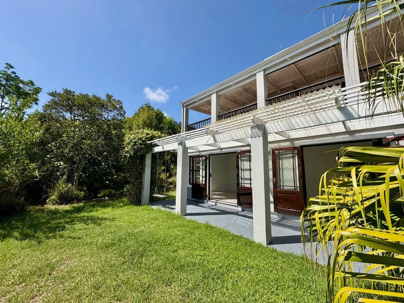 Rear view of the property featuring a covered patio with a pergola, upper-level balcony, and direct access to the garden through timber-framed doors.