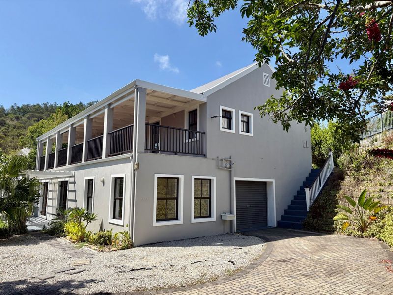 A well-maintained two-story house featuring a covered upper balcony, integrated garage, external staircase, and a neat paved driveway with gravel landscaping.