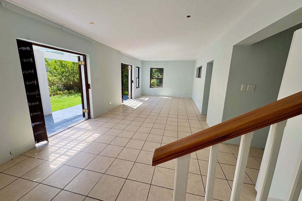 A spacious, empty living area featuring neutral tiled flooring, recessed lighting, and direct access to the garden through double doors.