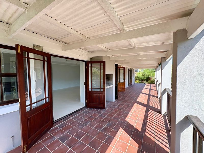 Spacious covered patio featuring terracotta tiled flooring, a built-in braai, and multiple timber-framed glass doors providing seamless access to the interior living space.
