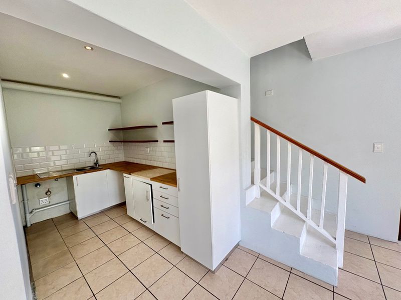 A compact kitchen area featuring white cabinetry, wooden countertops, and a subway tile backsplash, adjacent to an internal staircase with a wooden handrail.