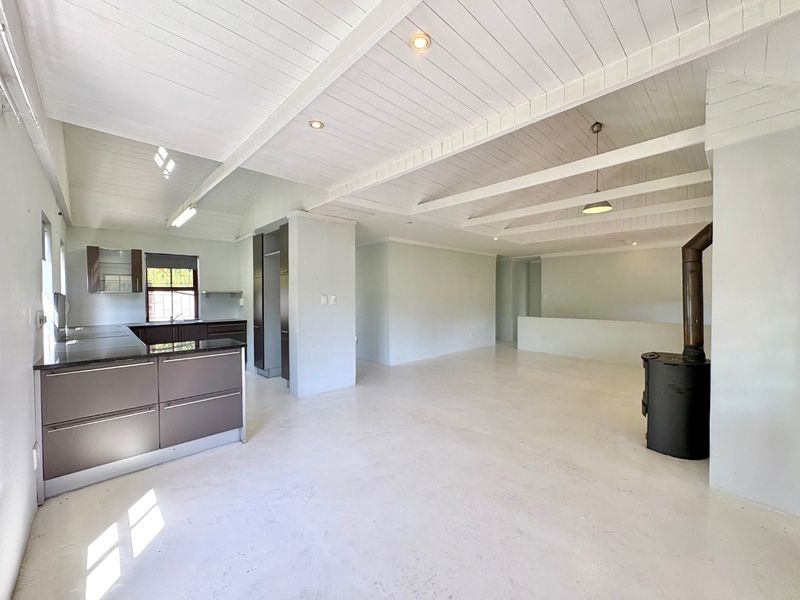 Spacious open-plan living area featuring a modern kitchen with granite countertops, exposed beam ceilings, and a cozy wood-burning fireplace.