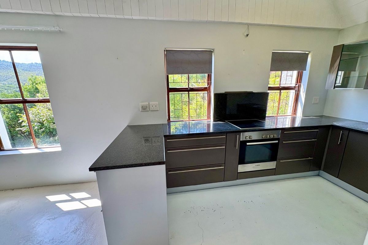 A functional kitchen featuring dark cabinetry, granite countertops, built-in oven and hob, set under a vaulted ceiling with scenic window views.