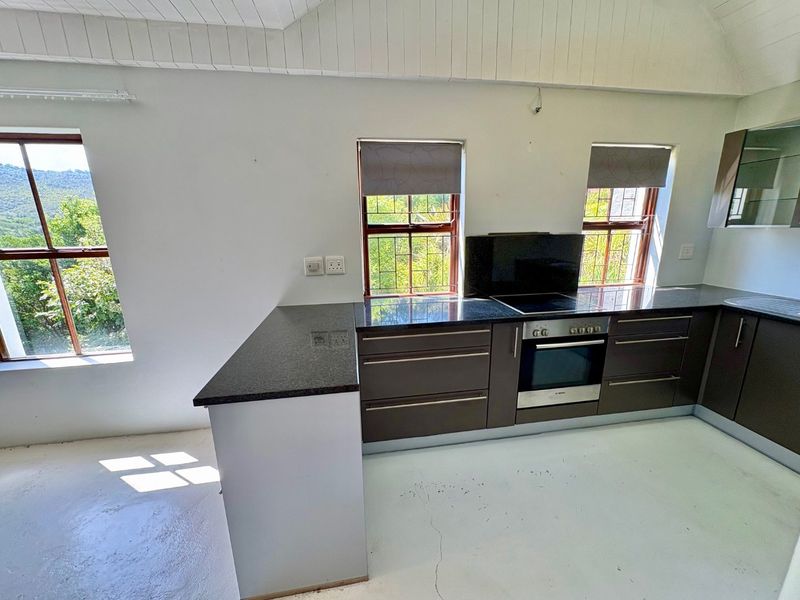 A functional kitchen featuring dark cabinetry, granite countertops, built-in oven and hob, set under a vaulted ceiling with scenic window views.