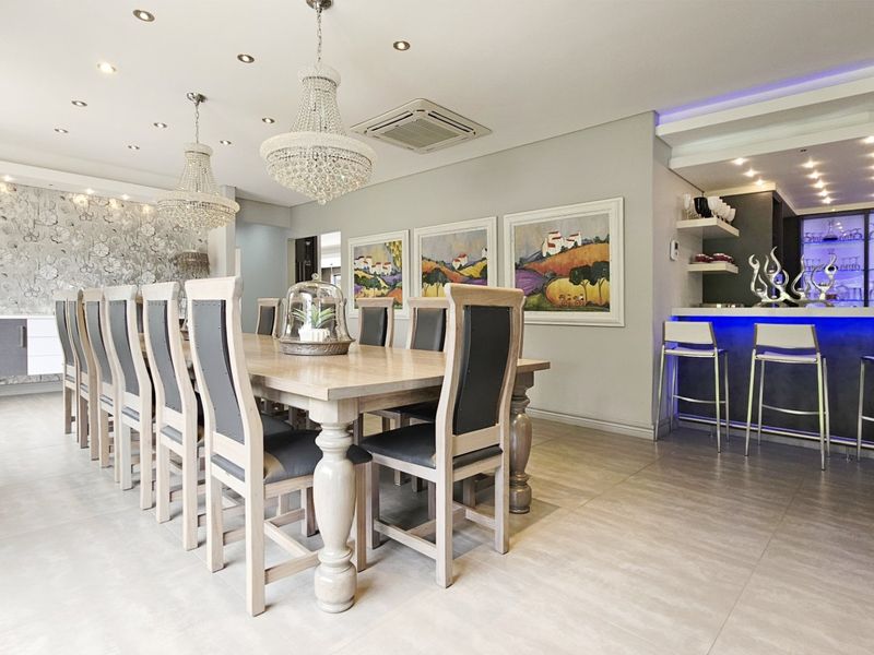 Spacious dining area featuring elegant crystal chandeliers, recessed lighting, tiled flooring, and a modern built-in bar with integrated accent lighting.