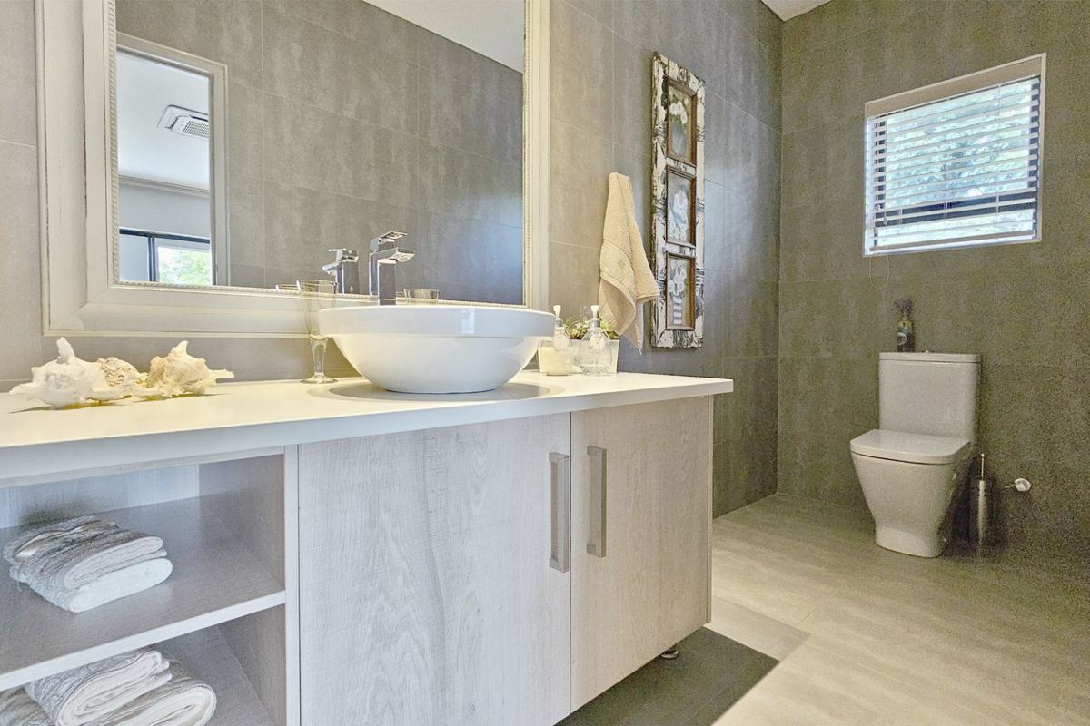 Modern bathroom featuring a vessel sink on a light wood vanity, large wall mirror, and neutral floor-to-ceiling wall tiles.