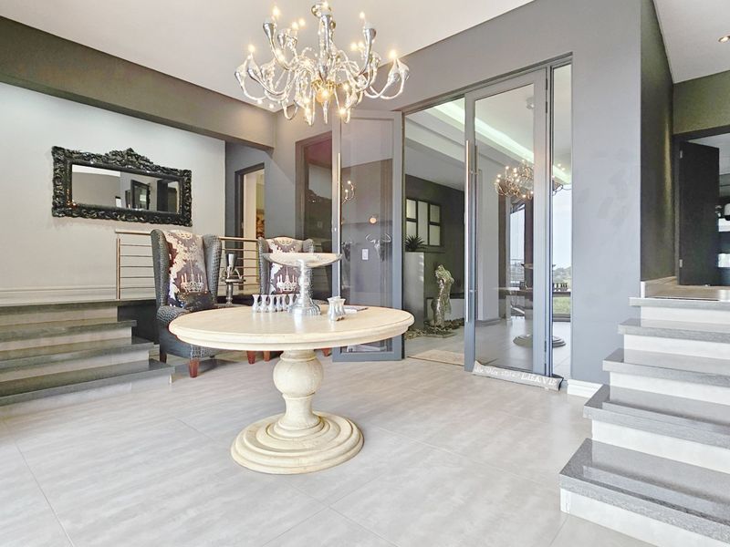 Spacious and elegant entrance hall featuring tiled flooring, a grand staircase, and modern glass panel doors leading to the living areas.