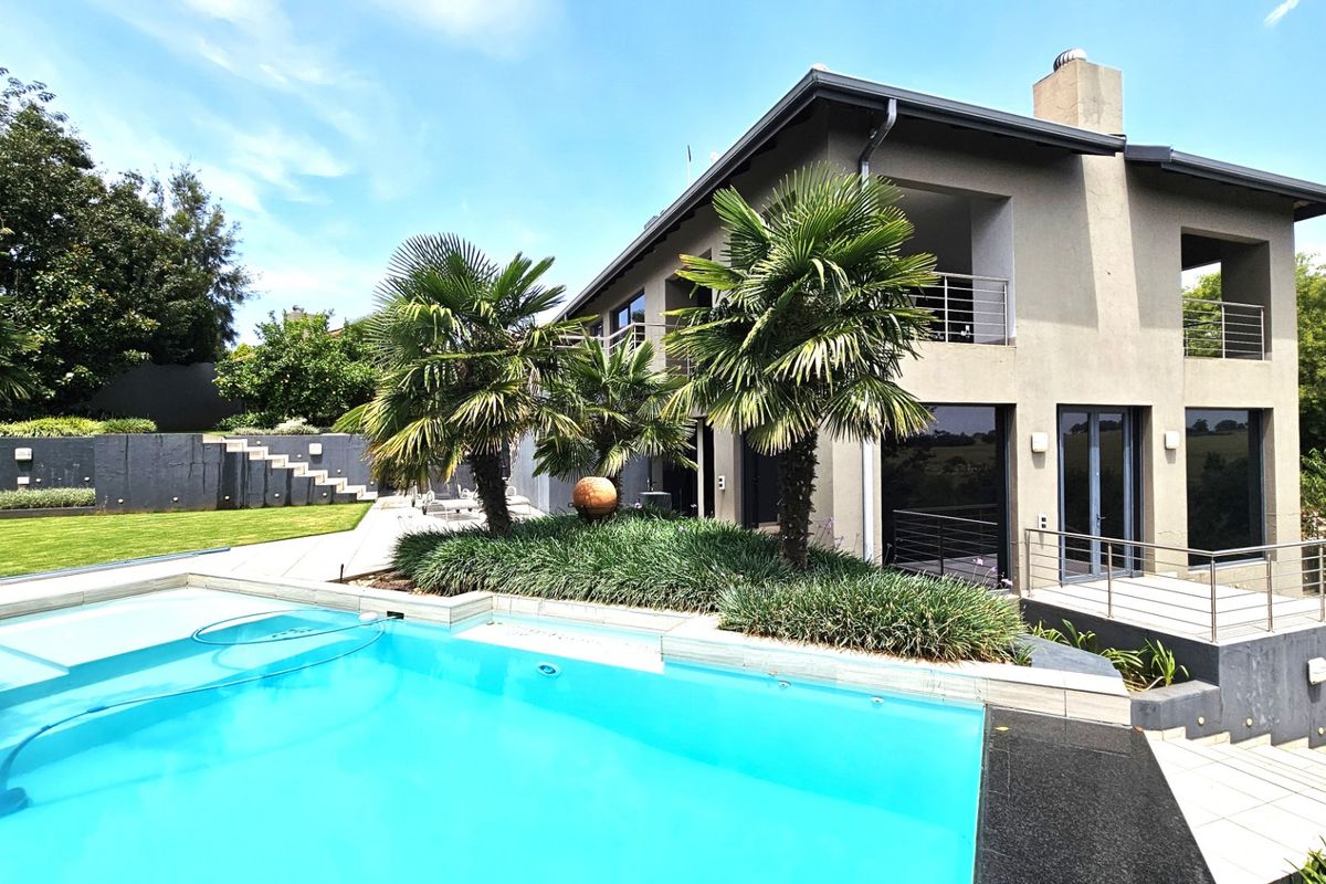 Rear view of a modern multi-story home featuring a swimming pool, landscaped garden, tiled patio, and upper-level balcony with stainless steel balustrades.