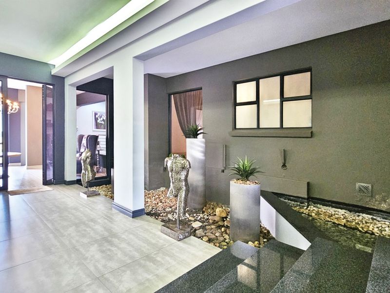 Modern entrance hall featuring large format floor tiles, recessed ceiling lighting, and an integrated indoor water feature with stone landscaping.