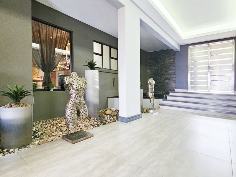 A spacious and modern entrance hall featuring large format floor tiles, recessed ceiling lighting, and a striking stone feature wall leading to the main entrance.