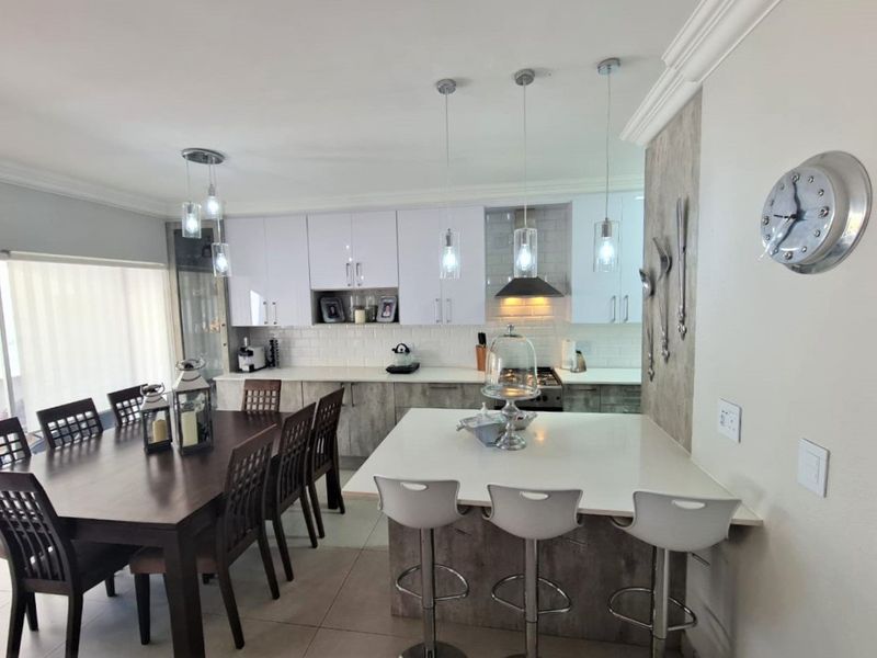 Modern open-plan kitchen and dining area featuring white cabinetry, stone countertops, subway tile backsplash, and a functional kitchen island with breakfast bar seating.
