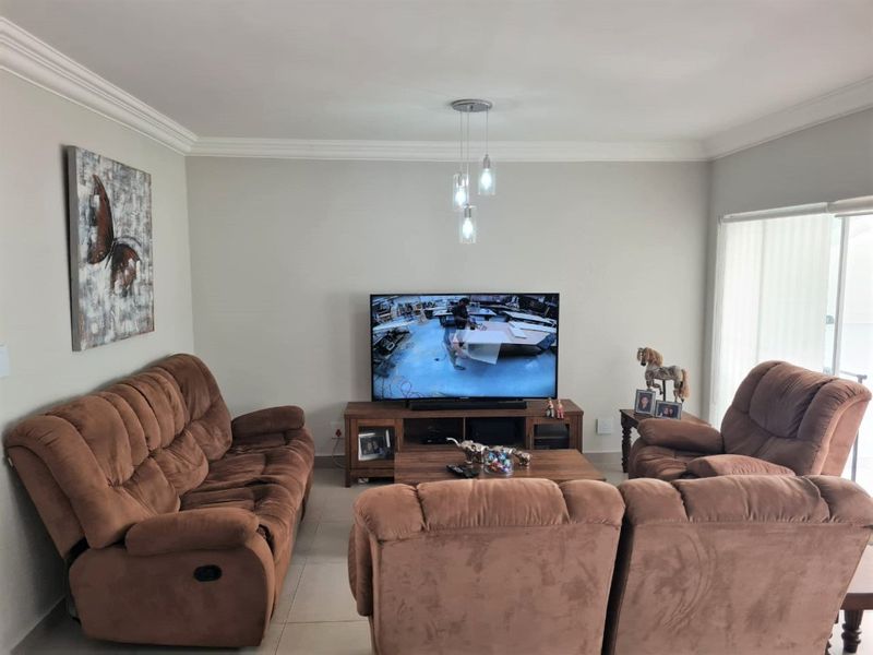 A comfortable living room featuring neutral walls, crown molding, tiled flooring, and a sliding glass door providing natural light.